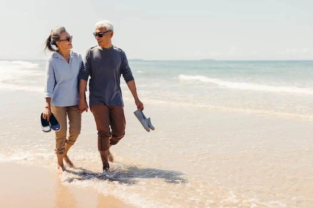 Romantic Senior couple strolling happily along the beach in the sunshine and bright sky. Retirement concept and happy life.